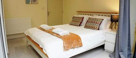 Une chambre à coucher avec un lit, des oreillers, une table de chevet, une lampe et une porte.