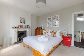 A bedroom with a large bed, a fireplace, a red nightstand, and a bookshelf. - Delightful 3BD Home with Garden in North London (London)