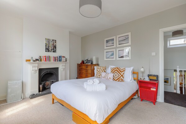 A bedroom with a large bed, a fireplace, a red nightstand, and a bookshelf.