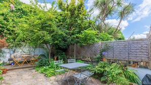 A patio area with a table and chairs, surrounded by lush greenery and a brick wall. - Delightful 3BD Home with Garden in North London (London)