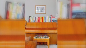 A room with a wooden piano, a bookshelf with various books, and a framed picture on the wall. - Delightful 3BD Home with Garden in North London (London)