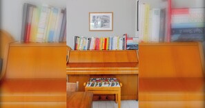 A room with a wooden piano, a bookshelf with various books, and a framed picture on the wall. - Delightful 3BD Home with Garden in North London (London)