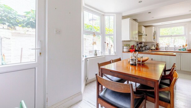 A kitchen with a wooden table and chairs, white cabinets, and a view of greenery outside. - Delightful 3BD Home with Garden in North London (London)