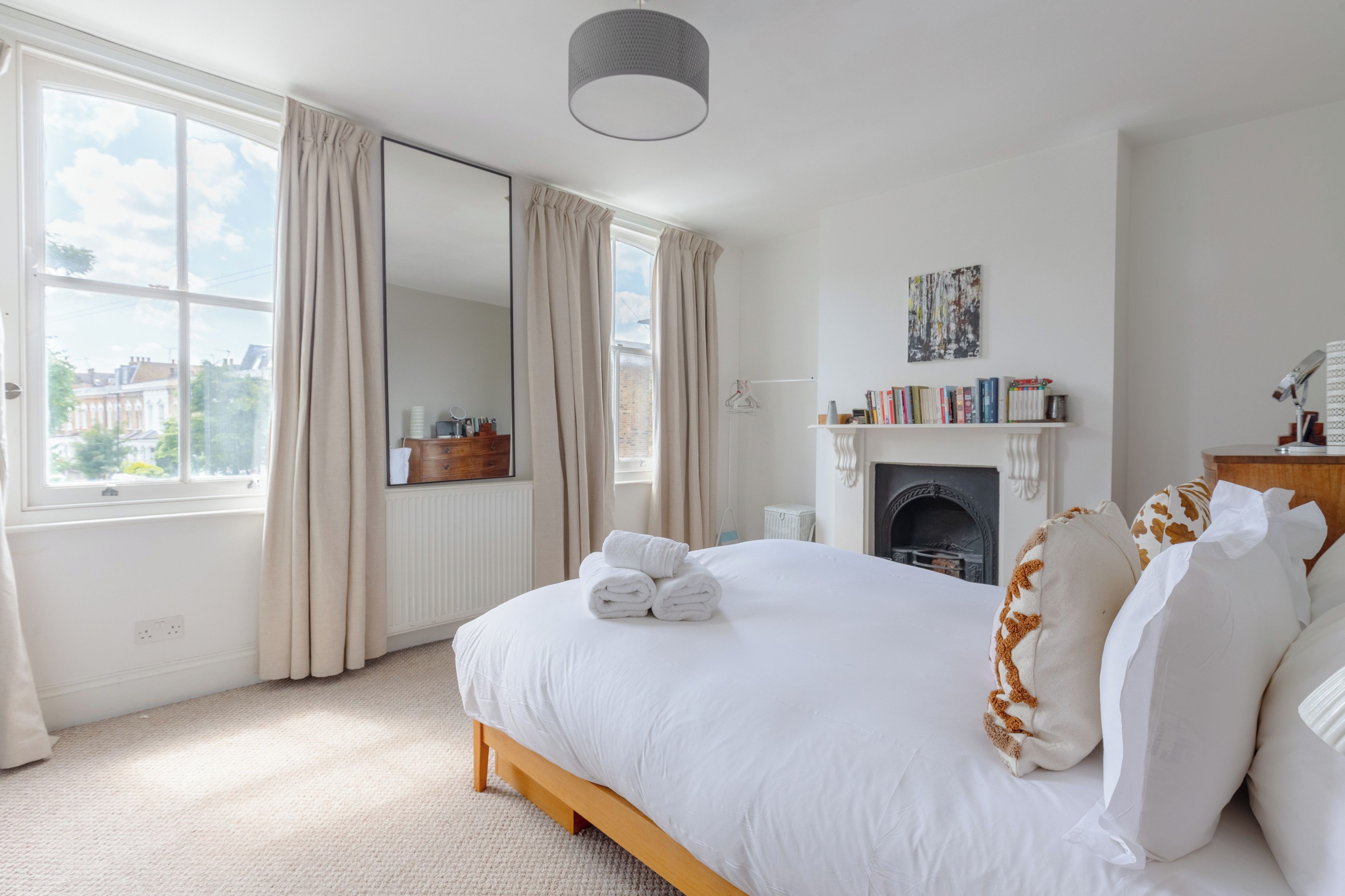 A bedroom with a large bed, a fireplace, a bookshelf, and a view of the outside.