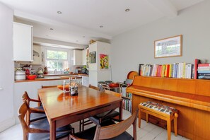 A dining area with a wooden table and chairs, a piano, and a bookshelf with books.