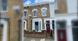 A row of terraced houses with white-framed windows and a red door. - Delightful 3BD Home with Garden in North London (London)
