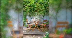 A garden with a wooden table and chairs, surrounded by lush greenery and a white wall. - Delightful 3BD Home with Garden in North London (London)