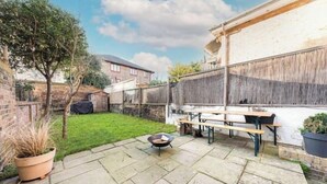 Un jardin avec un espace barbecue, une table de pique-nique et des plantes en pot.