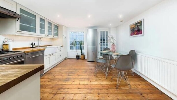 Une cuisine avec des meubles blancs, un plan de travail en bois, une table à manger avec des chaises et un réfrigérateur.