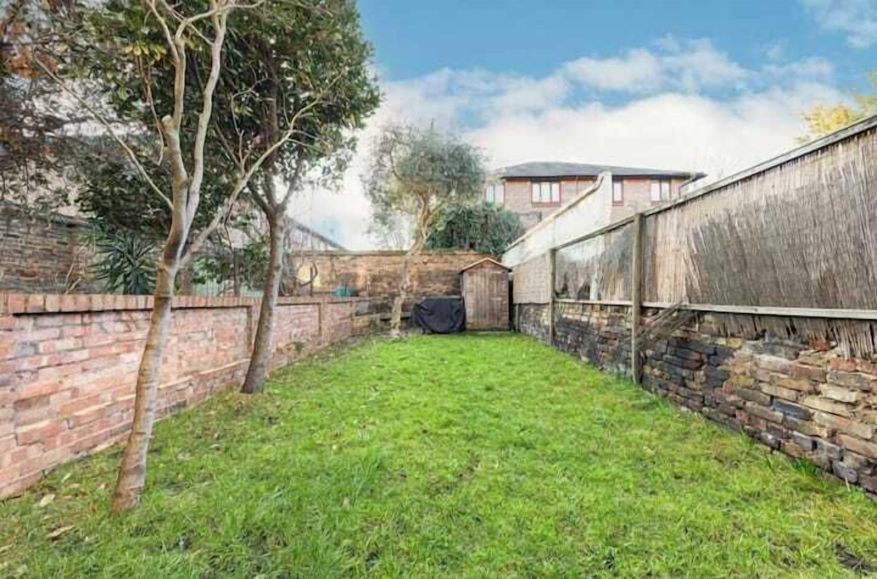 A backyard with a grassy lawn, brick walls, and a wooden fence.