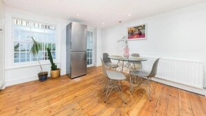 Une cuisine moderne dotée d’un réfrigérateur en acier inoxydable, d’un plancher en bois et d’un coin repas avec une table ronde et des chaises.