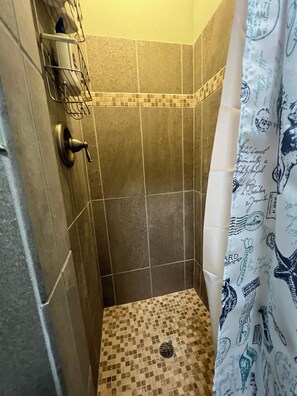 A shower area with tiled walls, a shower curtain with a pattern, and a metal rack with a towel.