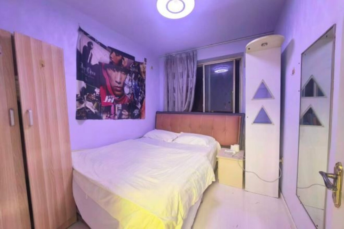 Un dormitorio con cama, mesita de noche, armario, ventana con cortinas y puerta con abertura triangular.