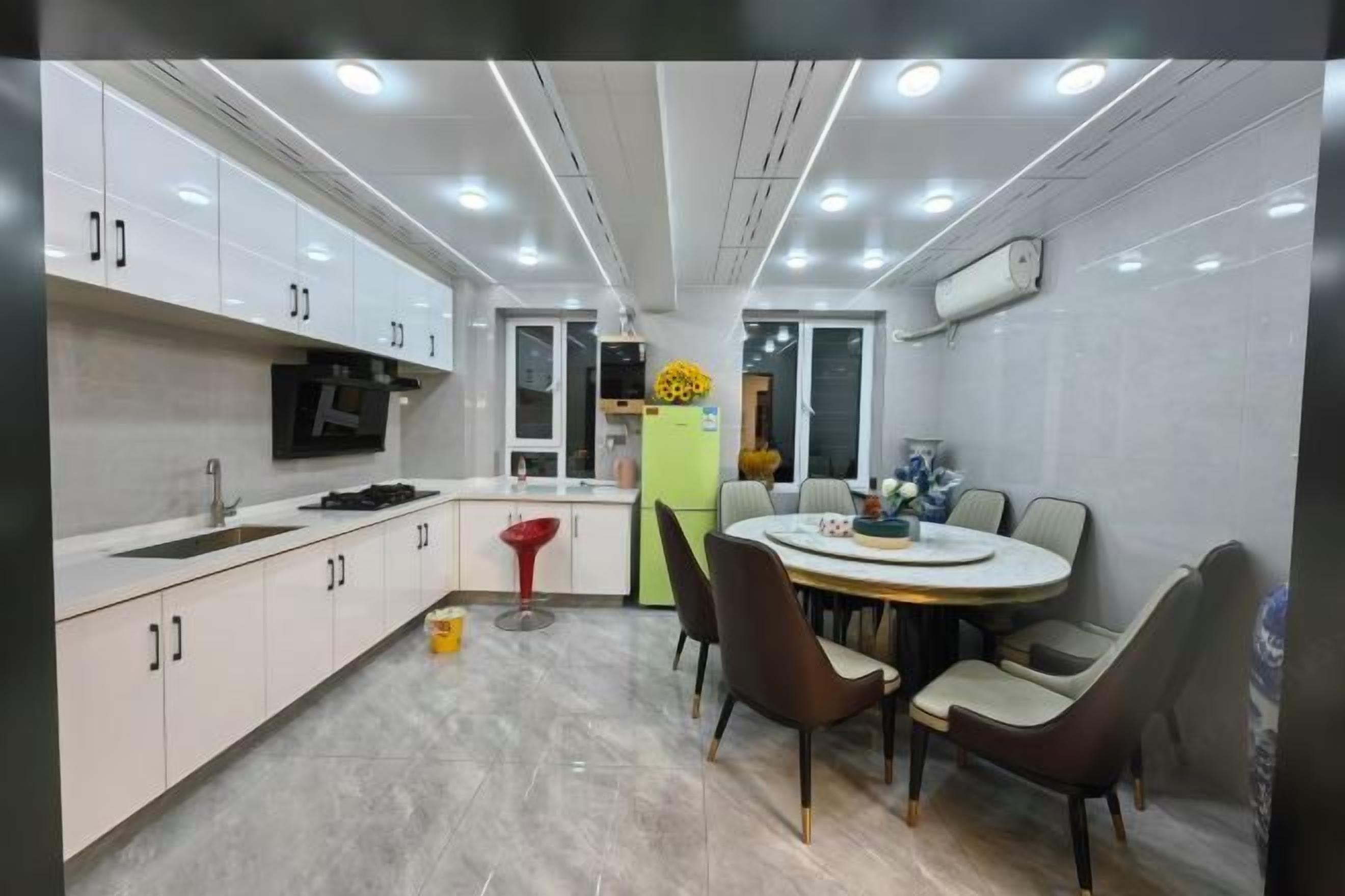 Een moderne keuken met witte kasten, een eethoek met een ronde tafel en stoelen, en een ingebouwde televisie.