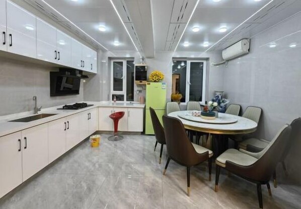 Cozinha moderna com armários brancos, área de refeições com mesa redonda e cadeiras, e forno embutido.