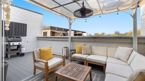Un patio exterior con una parrilla, muebles de madera y un cerramiento de vidrio.