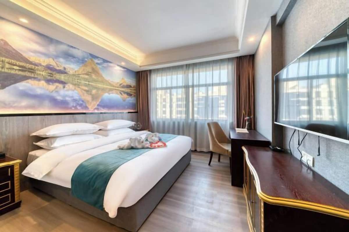 A hotel room with a large bed, a desk, a TV, and a mural of mountains.