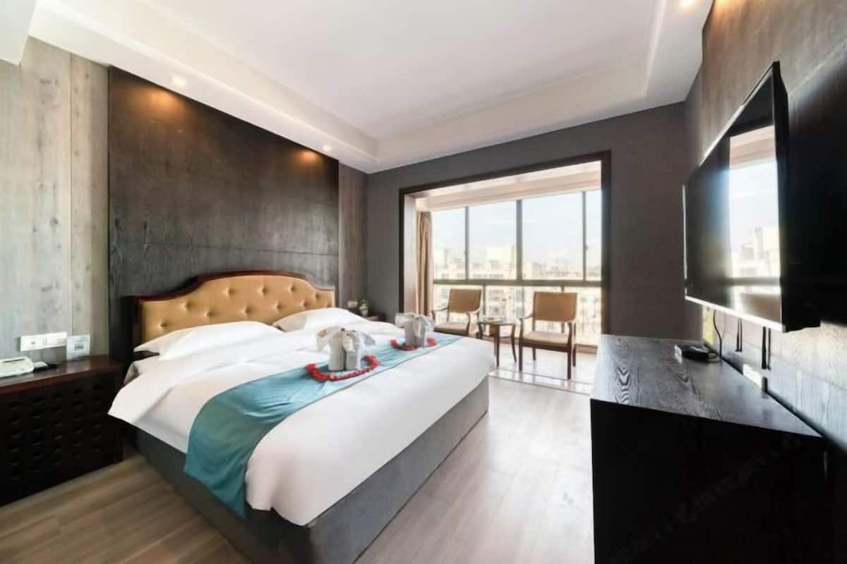 A hotel room with a large bed, a TV, a balcony with a city view, and a wooden headboard.