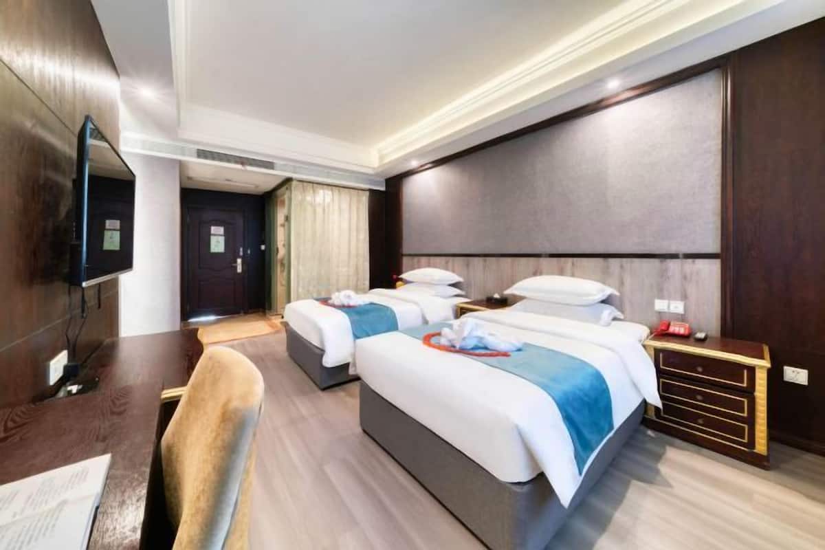 A hotel room with two beds, a desk, a chair, and a TV.