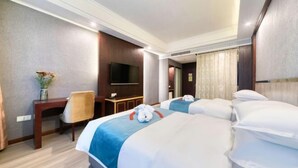 Ett hotellrum med två sängar, ett skrivbord, en stol, en TV och ett badrum med duschdraperi.