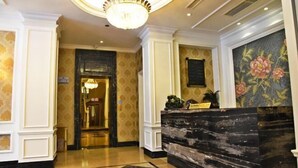 A lobby with a reception desk, a chandelier, and a floral painting on the wall. - Xindu Hotel (Wenzhou)