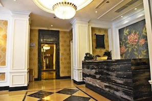 A reception area with a marble counter, a chandelier, and a door leading to another room. - Xindu Hotel (Wenzhou)
