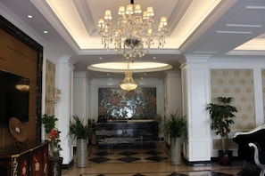 A lobby with a chandelier, a reception desk, and potted plants. - Xindu Hotel (Wenzhou)