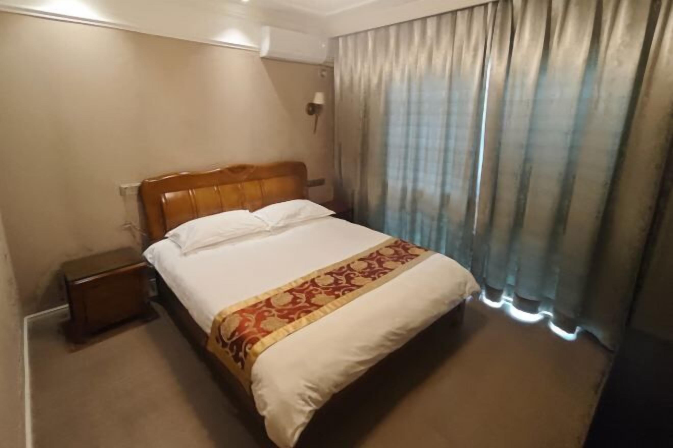 A hotel room with a bed, a nightstand, a lamp, and a window with curtains.