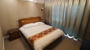 A hotel room with a bed, a nightstand, a lamp, and a window with curtains.