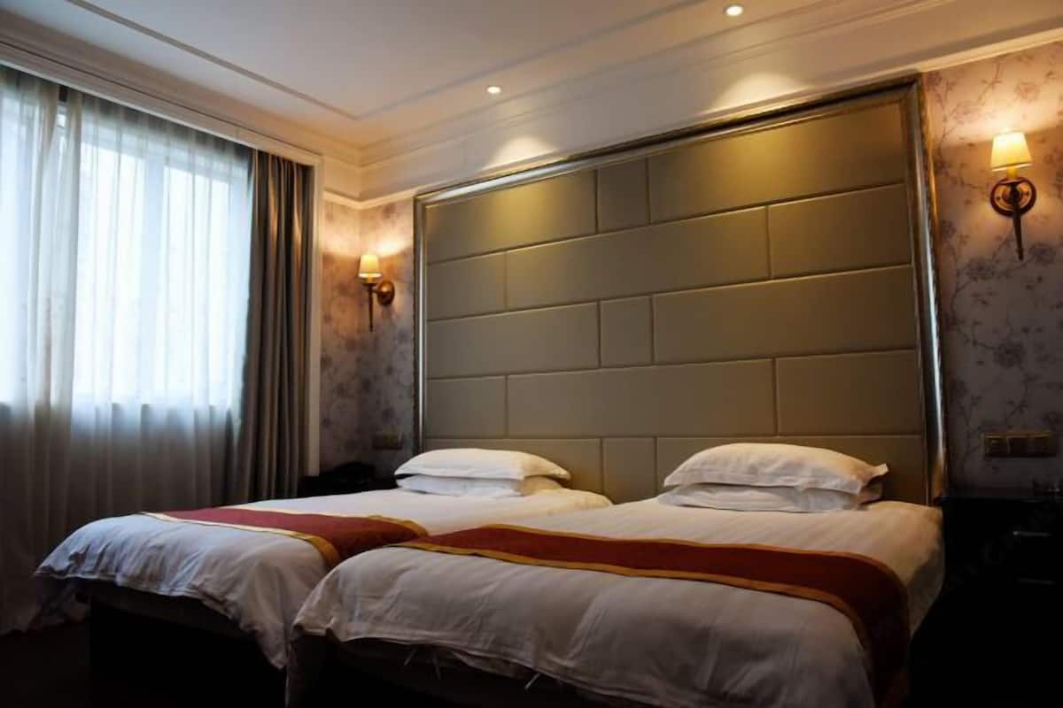A hotel room with two beds, a large padded headboard, and a window with curtains.