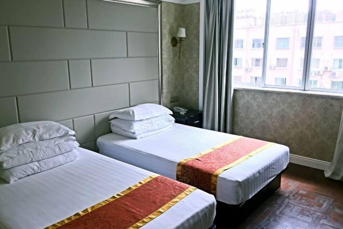A hotel room with two beds, a nightstand, a lamp, and a window with curtains.