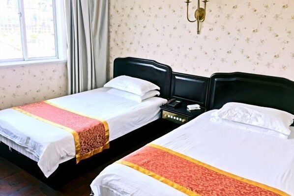 A hotel room with two single beds, each with a white and red bedspread. There is a nightstand between the beds with a phone and a lamp. The room has floral wallpaper and a window with curtains. - Xindu Hotel (Wenzhou)