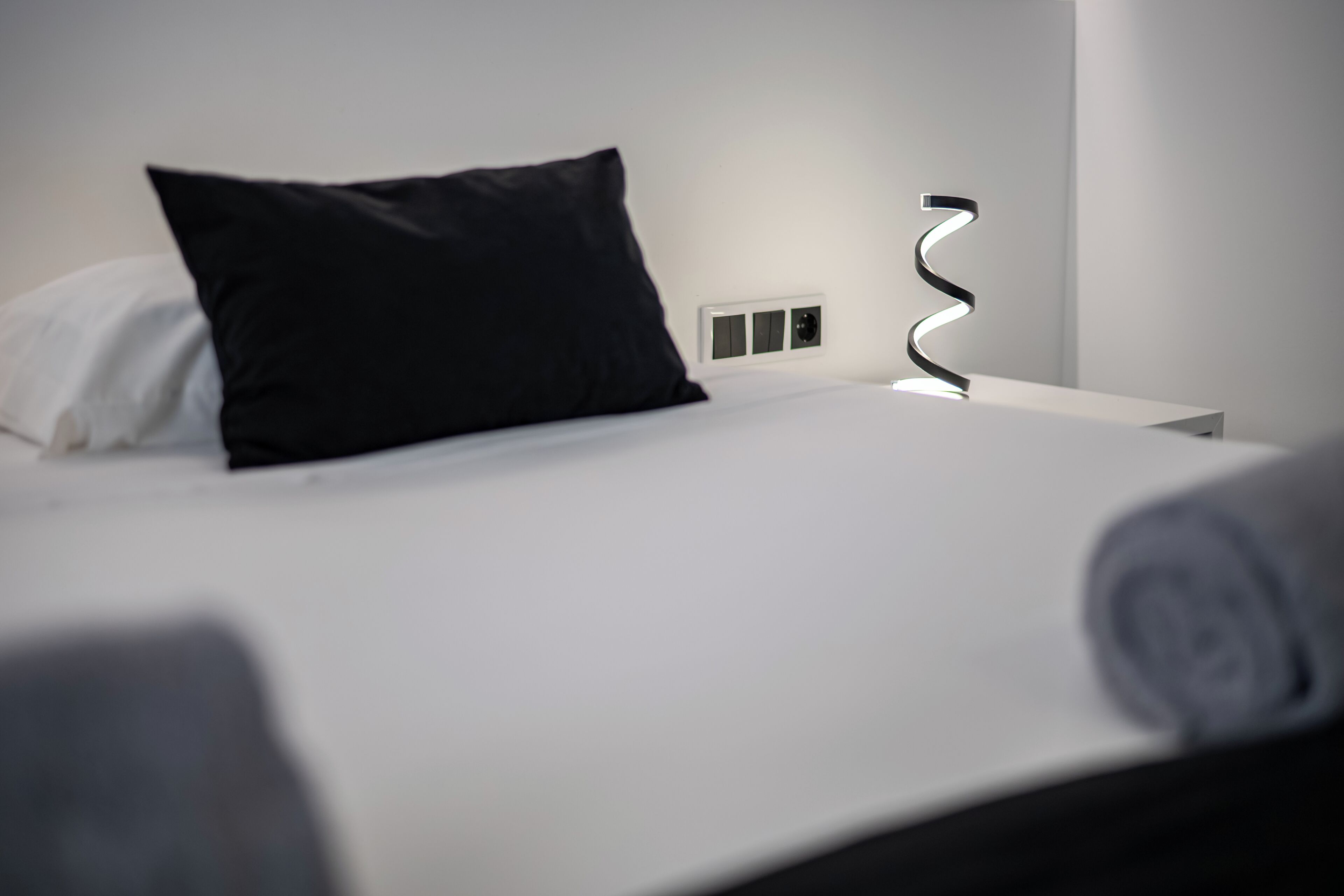 A neatly made bed with a black pillow, a white pillow, and a white headboard.