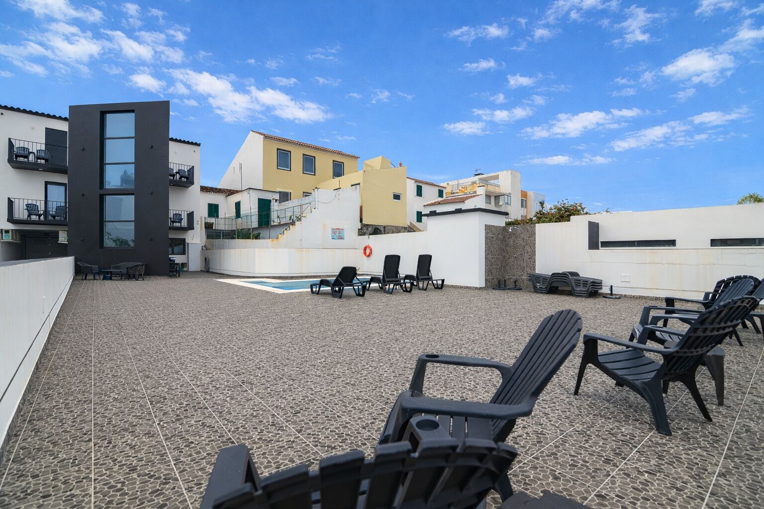 A rooftop terrace with a pool, lounge chairs, and a view of buildings.