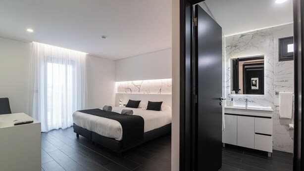 A modern hotel room with a bed, bedside table, and a bathroom with a marble sink. - The Rock Hostel (Ponta Delgada)