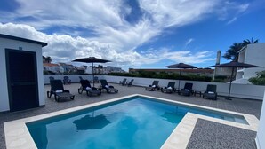 A rooftop pool area with lounge chairs and umbrellas, surrounded by a white wall and buildings in the background. - The Rock Hostel (Ponta Delgada)