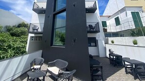 A modern building with a large glass window, outdoor seating, and a clear blue sky. - The Rock Hostel (Ponta Delgada)
