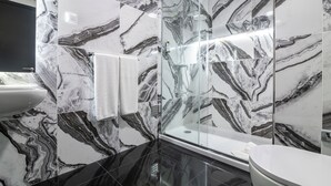 A modern bathroom with marble walls, a glass-enclosed shower, and a white sink. - The Rock Hostel (Ponta Delgada)