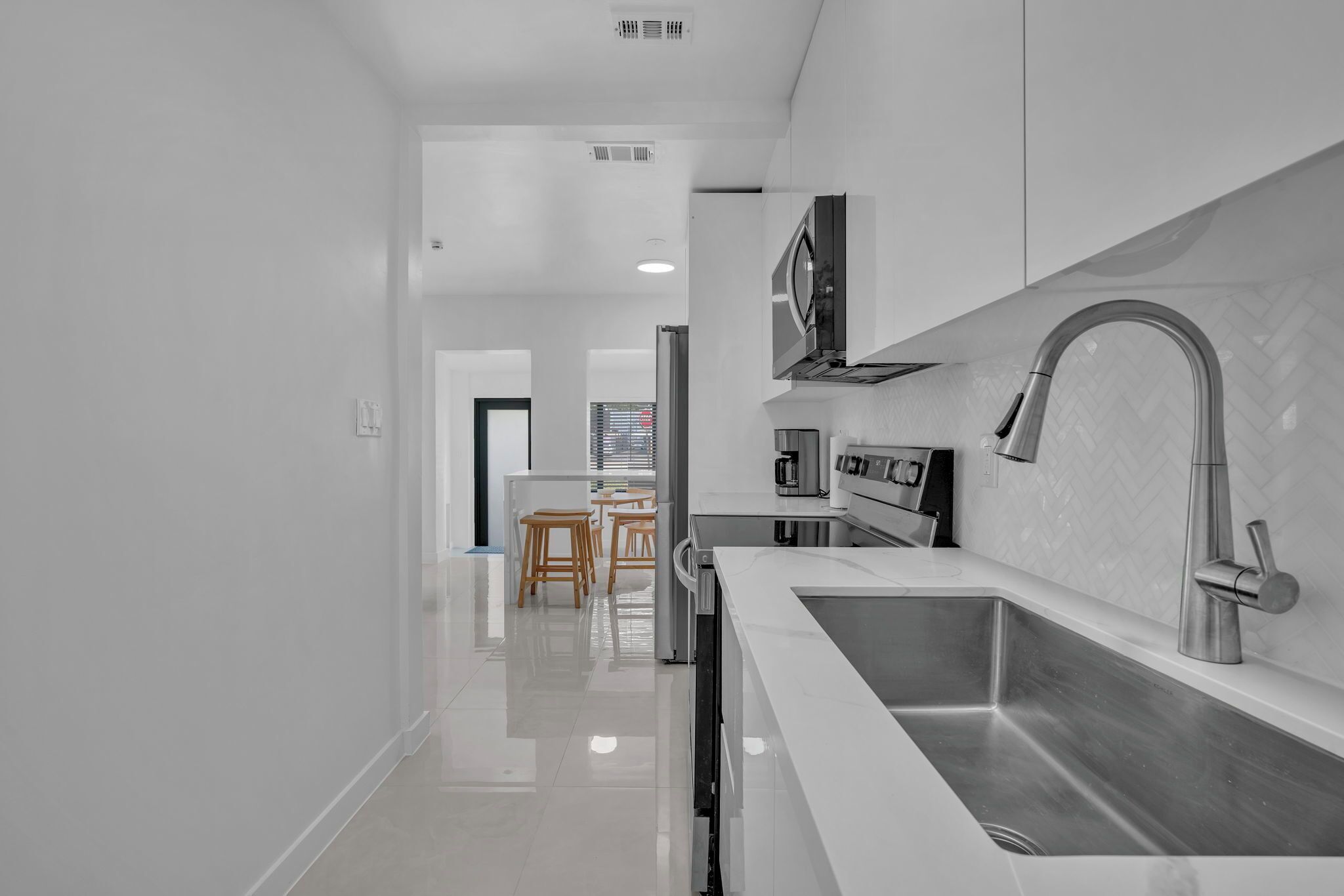A modern kitchen with white cabinetry, stainless steel appliances, and a large sink.
