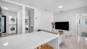 Una cocina moderna con encimera de mármol, lavadora y televisor de pantalla plana.