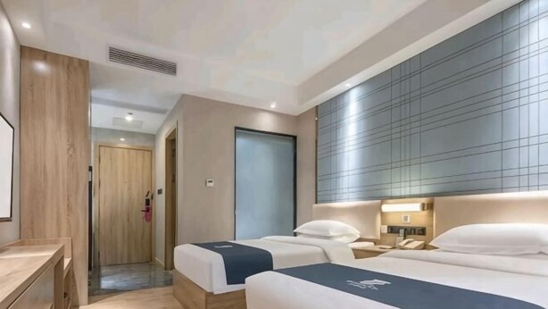 Une chambre d’hôtel avec deux lits, un bureau et une grande fenêtre avec des stores.