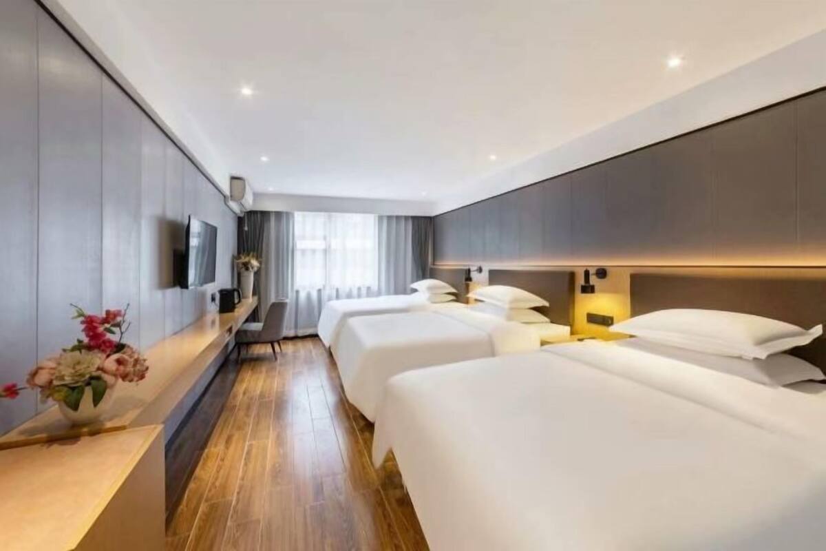 Habitación de hotel con dos camas, un televisor, un escritorio con un florero y una ventana con cortinas.