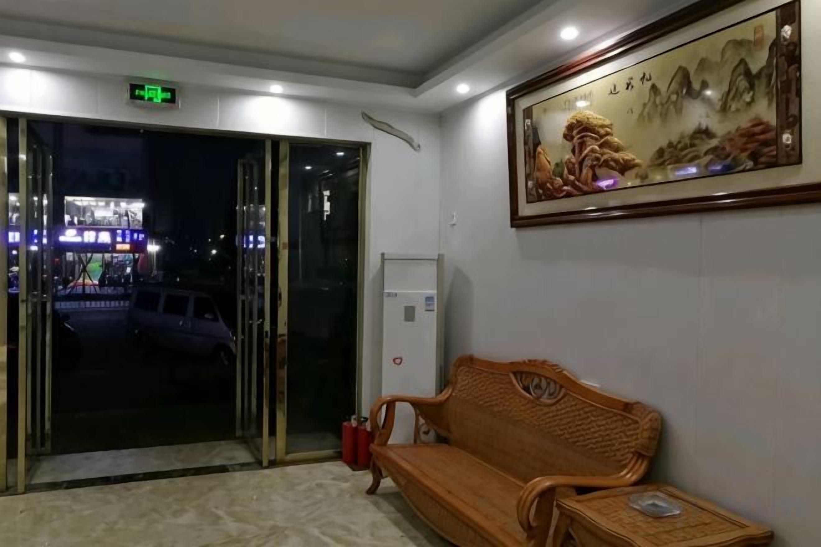 A hotel lobby with a reception desk, a sofa, a painting on the wall, and a door leading outside.