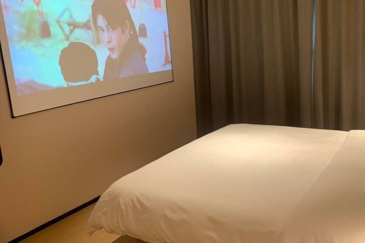 Una habitación de hotel con una cama, un televisor montado en la pared y una cortina.