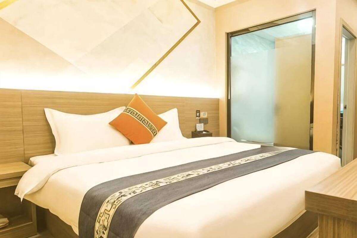 Una habitación de hotel con cama, mesitas de noche, un espejo y una puerta.