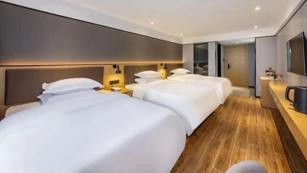 Ein Hotelzimmer mit drei Betten, Holzboden, einem großen Spiegel und einer Kaffeemaschine.