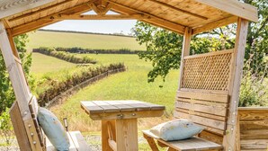 A wooden pergola with a table and benches, overlooking a rural landscape with fields and a fence. - Cosy Luxury Owls Roost Hut With Private Hot Tub (Umberleigh)