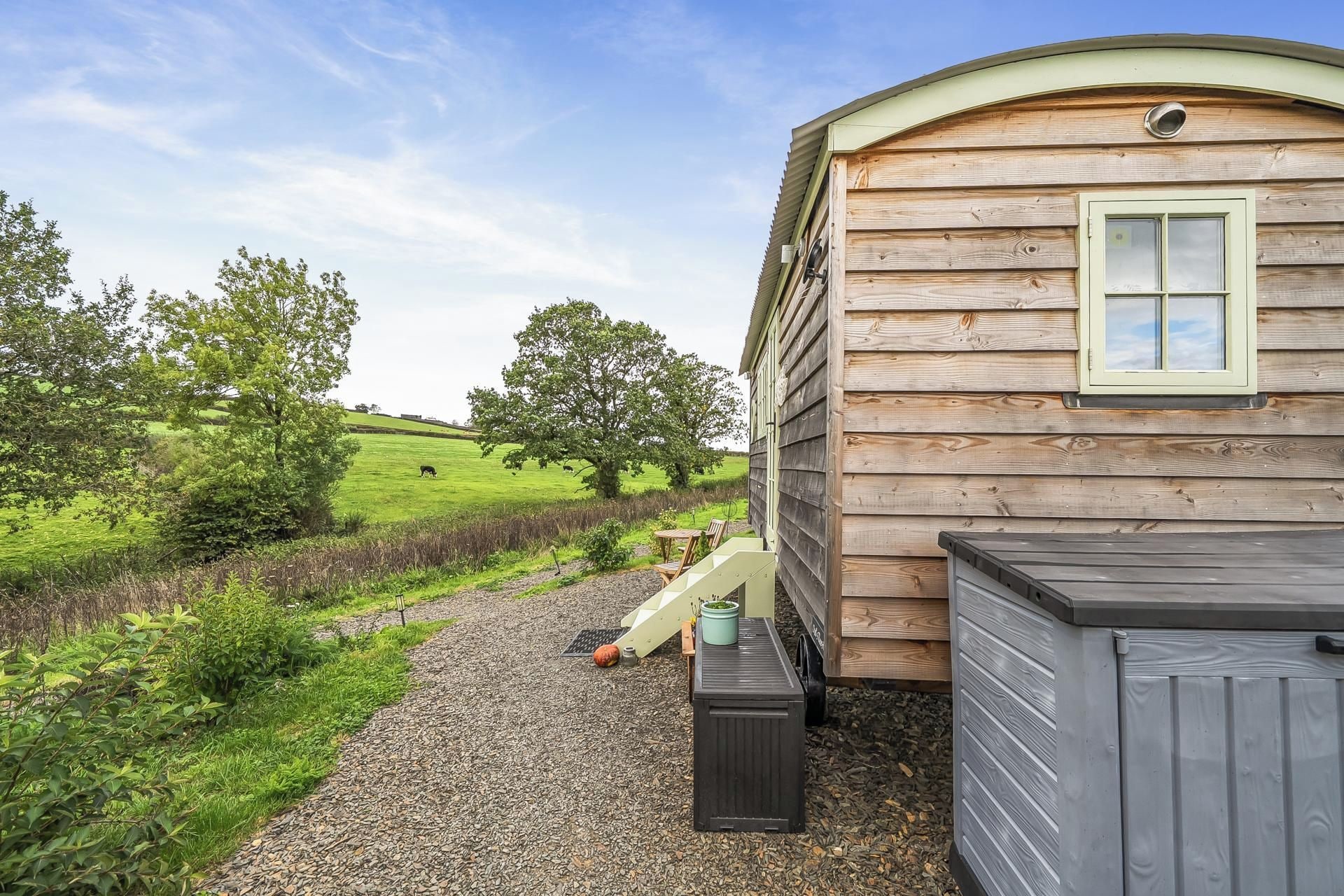 A wooden cabin with a window, a gravel path, and a green field in the background.