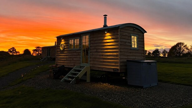 A wooden cabin with a chimney, a small porch, and a shed. - Cosy Luxury Owls Roost Hut With Private Hot Tub (Umberleigh)