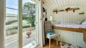 A bedroom with a bed, a chair, a small table, and a window with a view of the outdoors. - Cosy Luxury Owls Roost Hut With Private Hot Tub (Umberleigh)